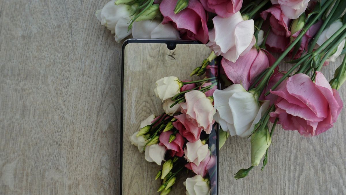 A smartphone lying beside pink and white flowers on a wooden table